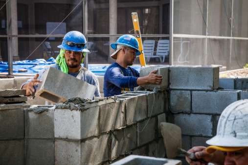 Construction workers at a job site in SW Florida are building a concrete block wall.